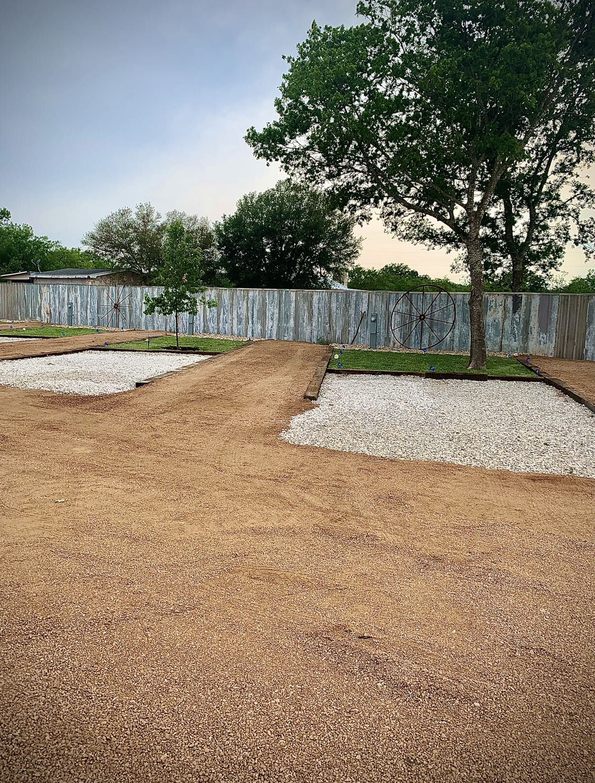Freshly built RV lots with white gravel pads, timber edging, small grass yards and an antique wagon wheel against the metal privacy fence