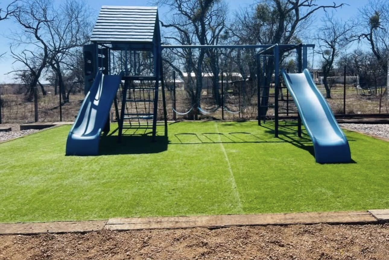 The Z-Ranch playground: a blue playset with two slides, swings and monkey bars on soft turf