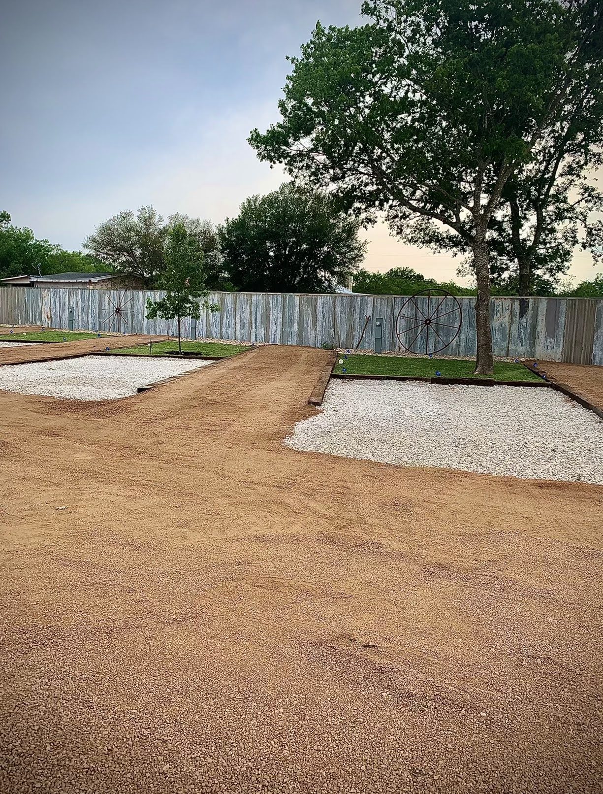 Freshly graded gravel RV site pads beside a privacy fence and shade tree
